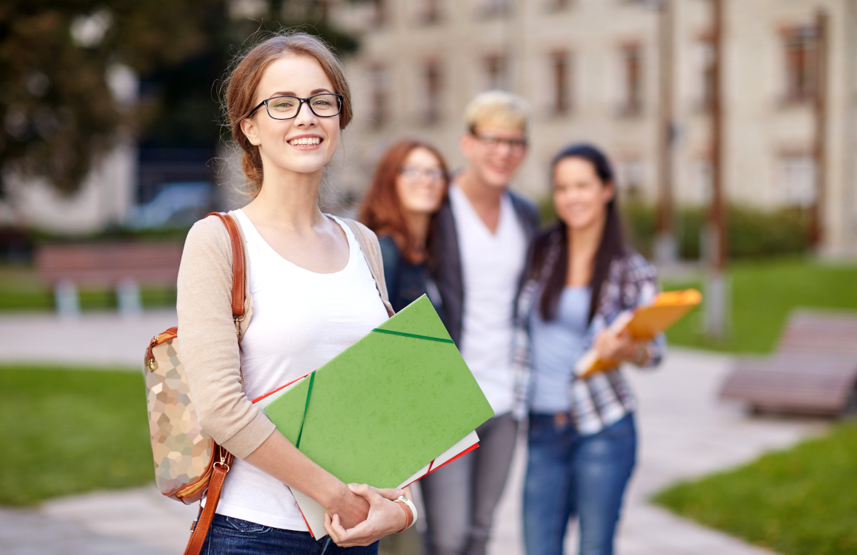 A college aged girl smiling while holding a green folder